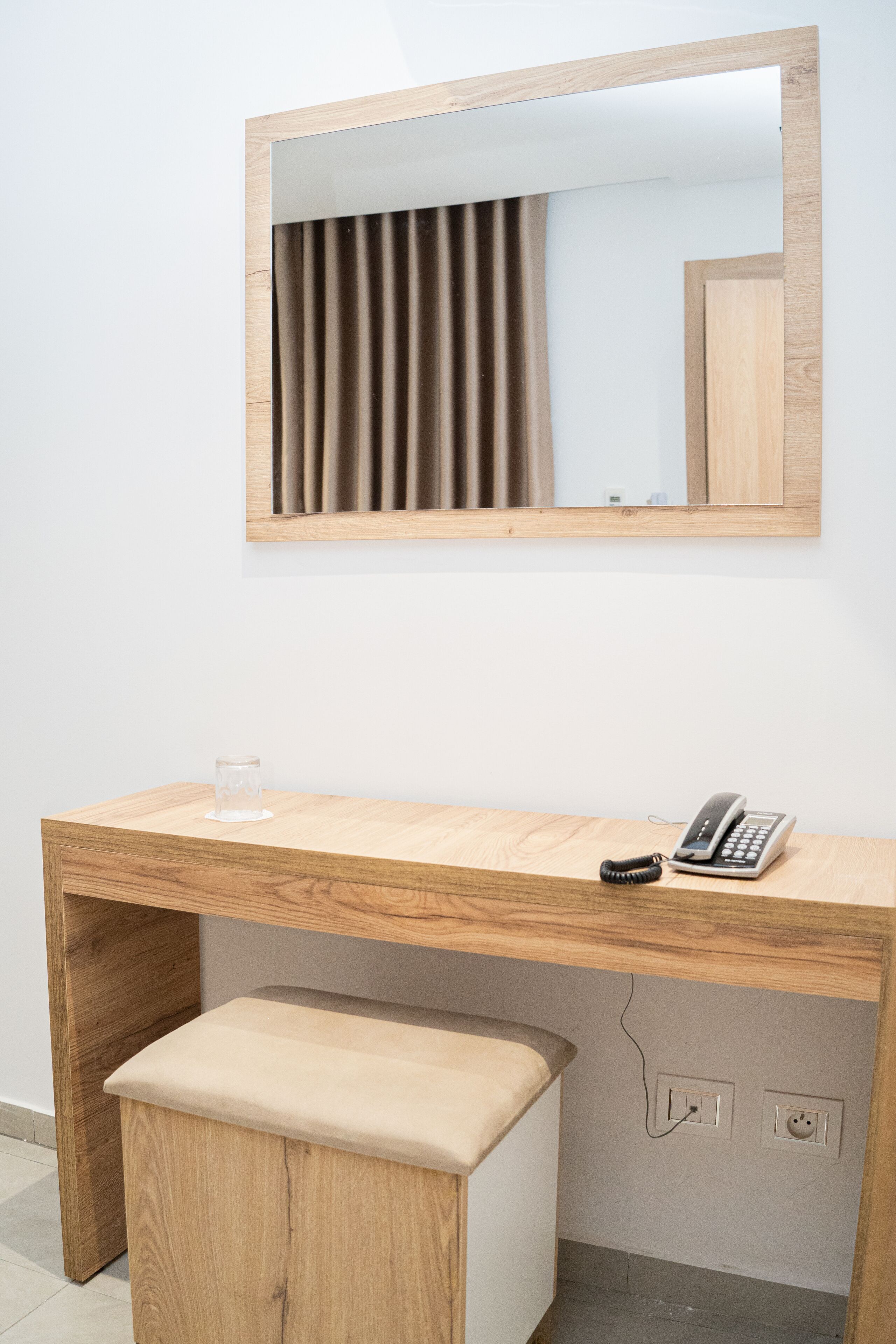 A wooden desk with a telephone and a glass.