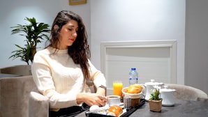A person sitting at a table with a tray containing food, a drink, and a small plant. - Hôtel Suisse (Tunis)
