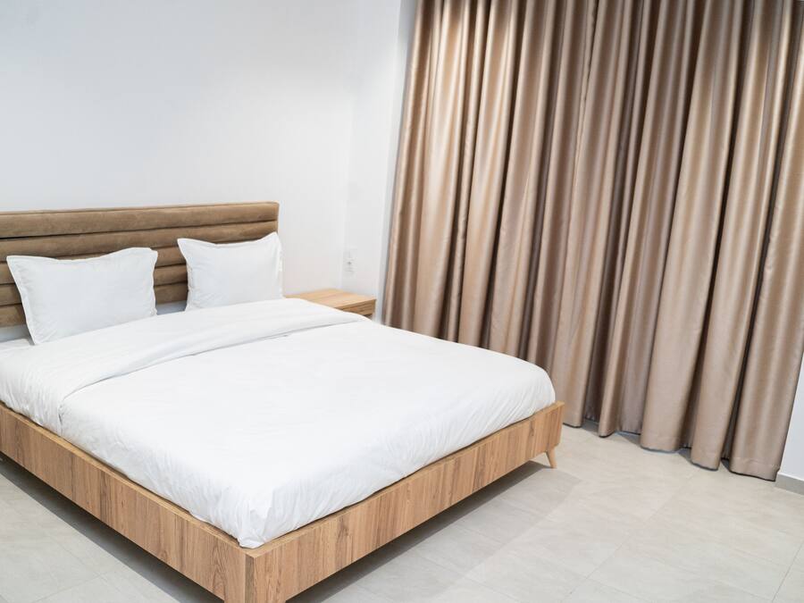 Une chambre moderne avec un cadre de lit en bois, du linge de lit blanc et un rideau en arrière-plan.