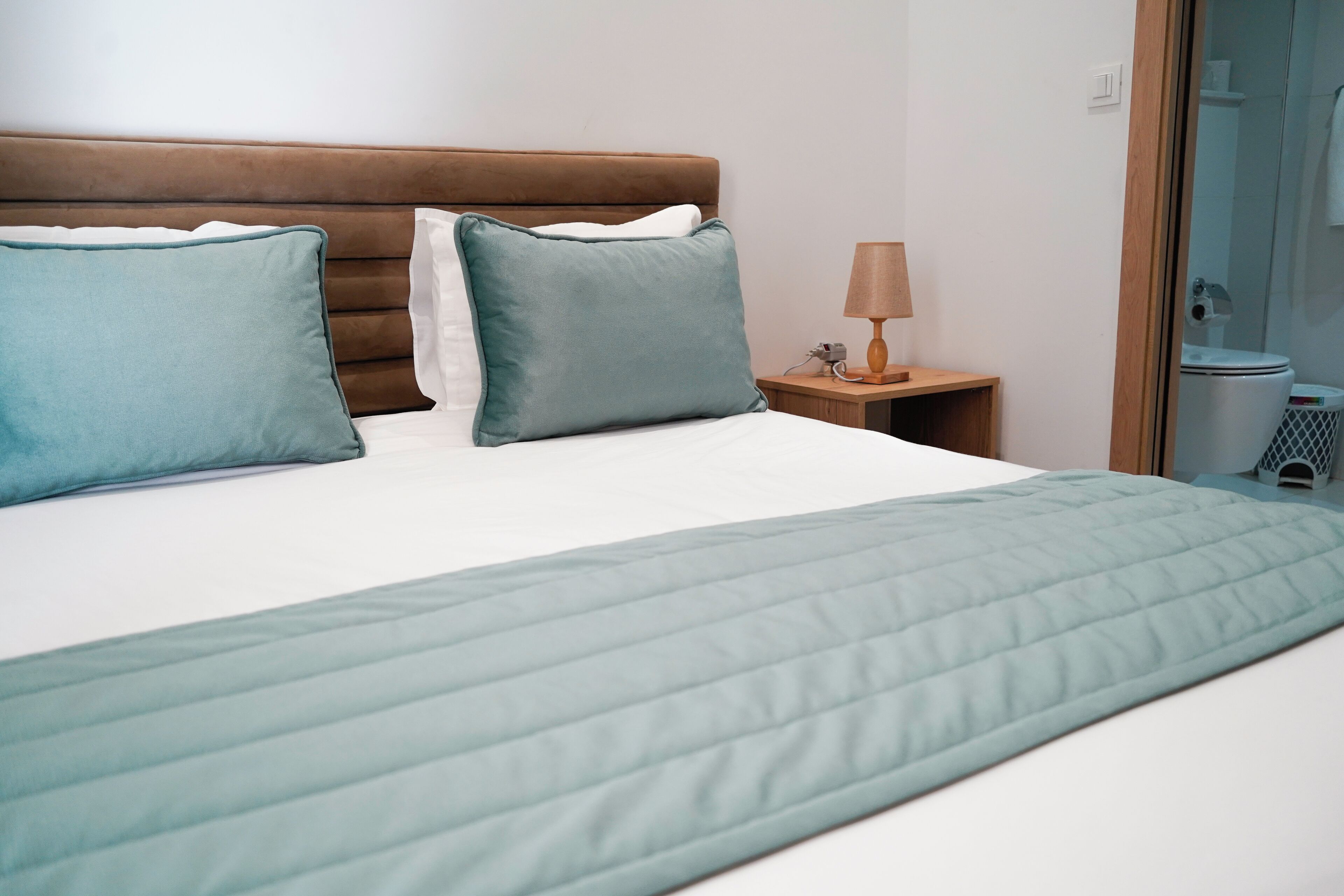 A hotel room with a bed, pillows, a nightstand, a lamp, and a shower area.