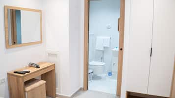Une salle de bain moderne avec un meuble-lavabo en bois, un miroir et des toilettes visibles à travers une porte en verre.