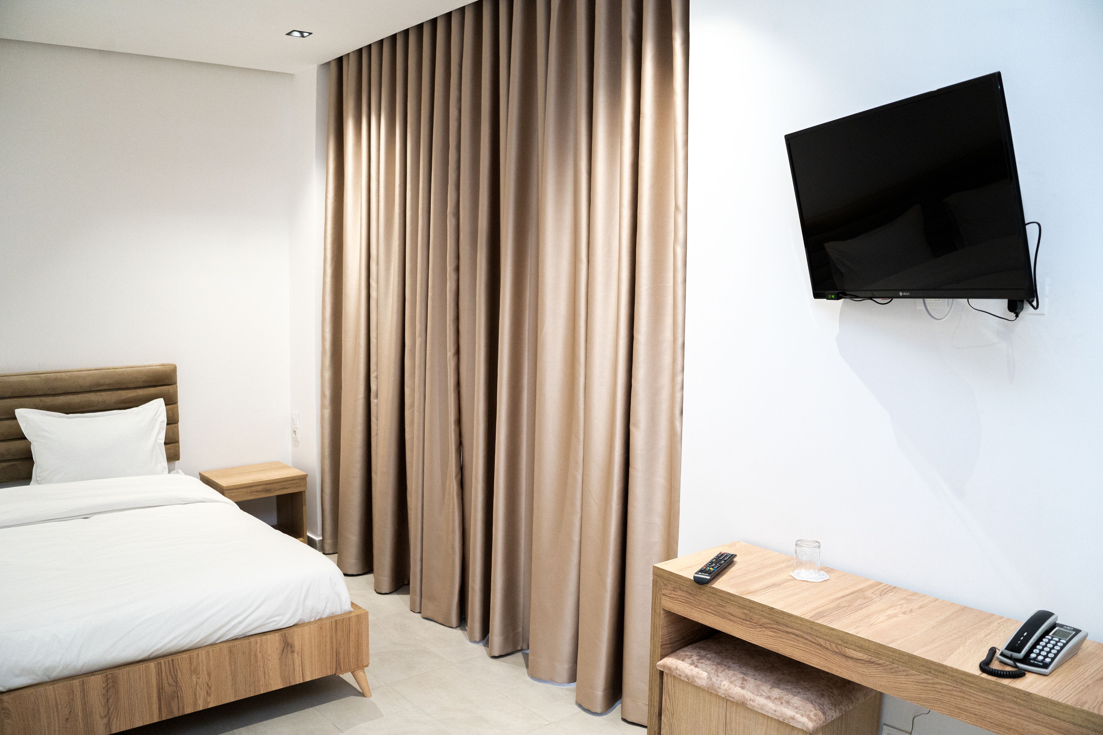 A modern hotel room with a bed, a desk, a TV, and a curtain.