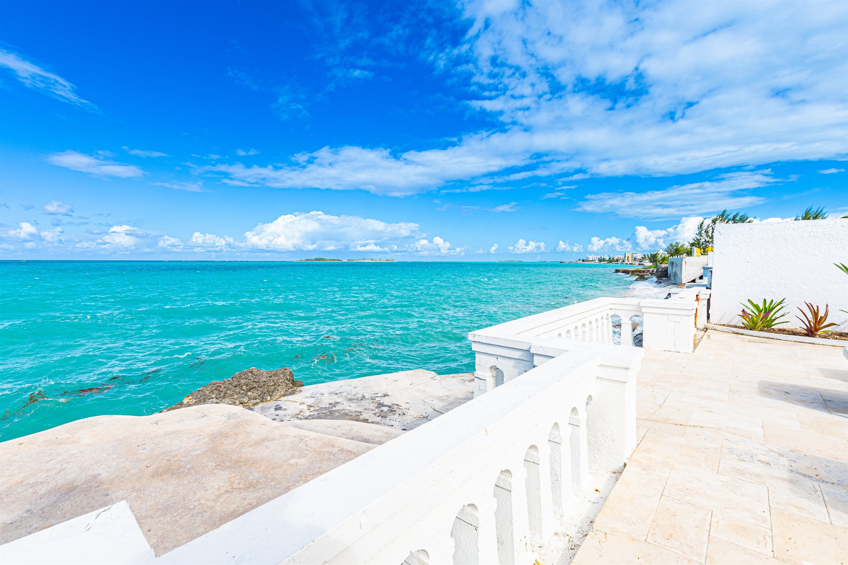 Une promenade en bord de mer mène à un bâtiment blanc d’où l’on peut admirer la mer turquoise et les îles lointaines.