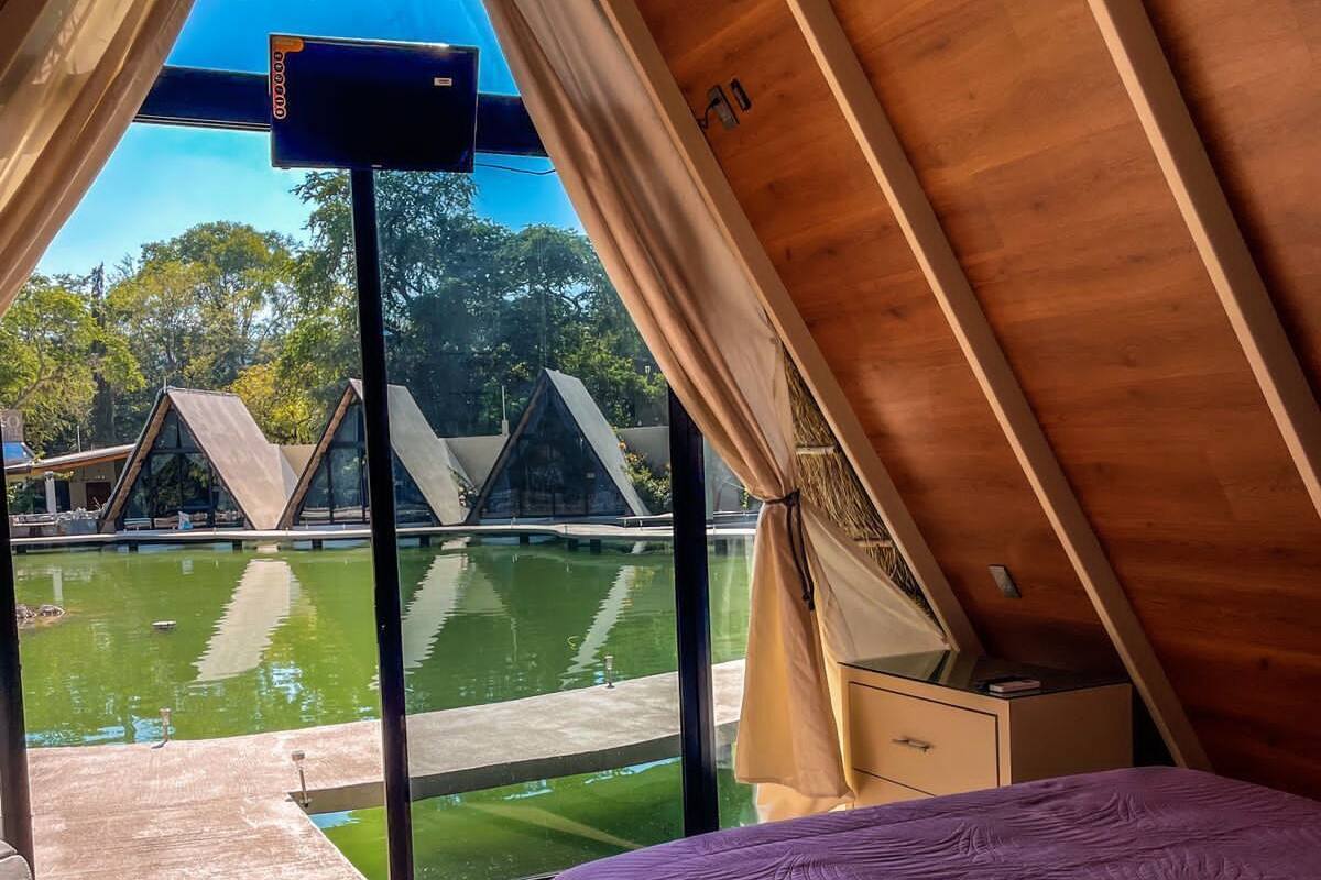 A bedroom with a large window, a bed, and a view of a swimming pool and buildings.