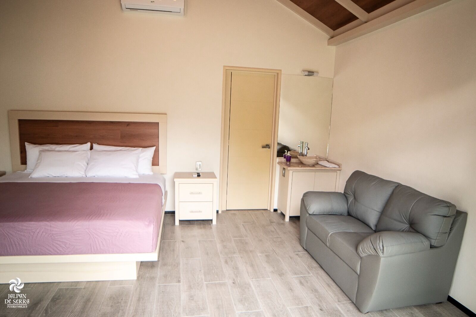 A bedroom with a bed, bedside table, nightstand, and a gray sofa.