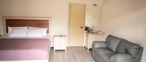 A bedroom with a bed, bedside table, nightstand, and a gray sofa.