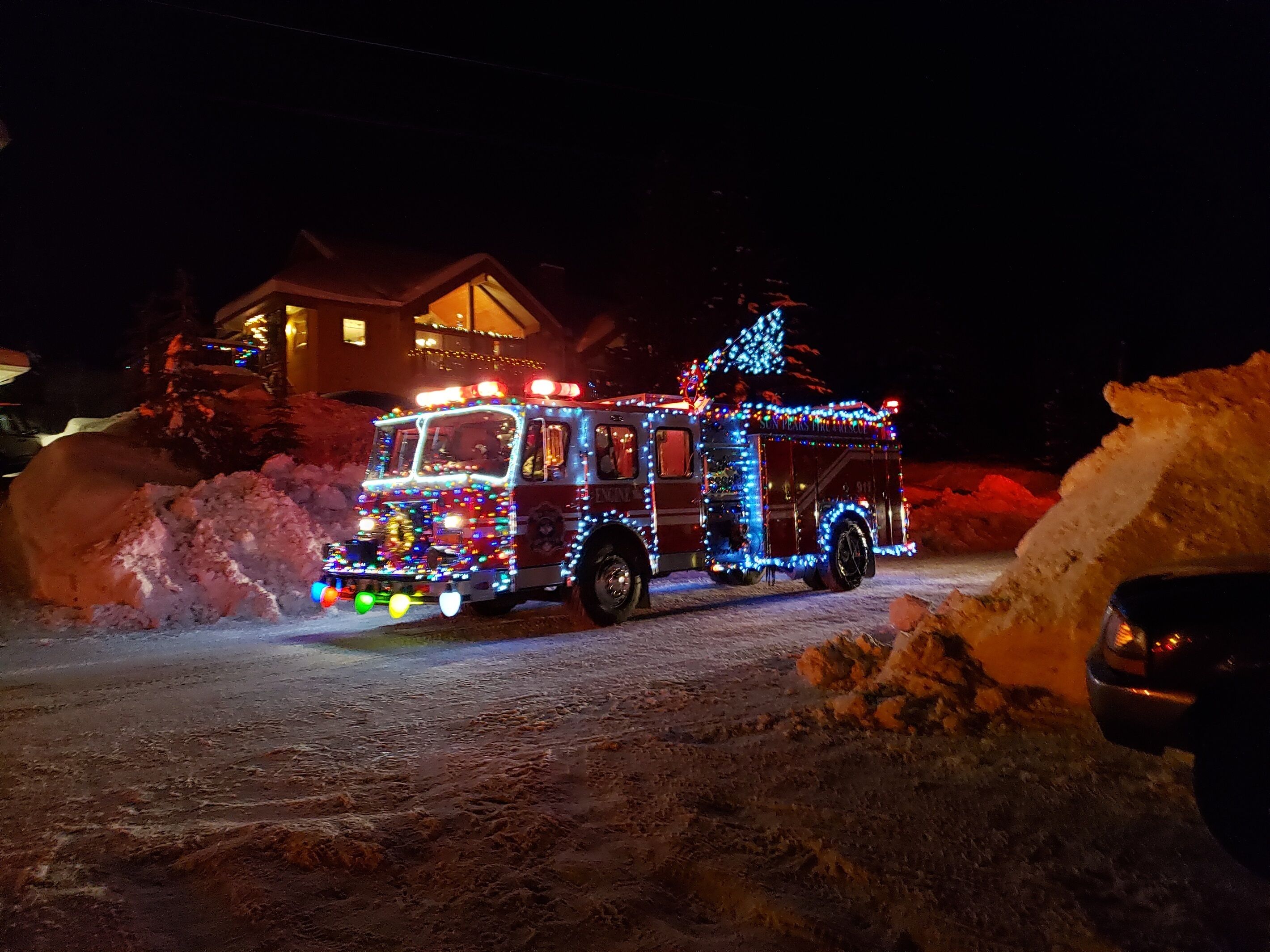 A snow-covered road with a fire truck decorated with colorful lights.