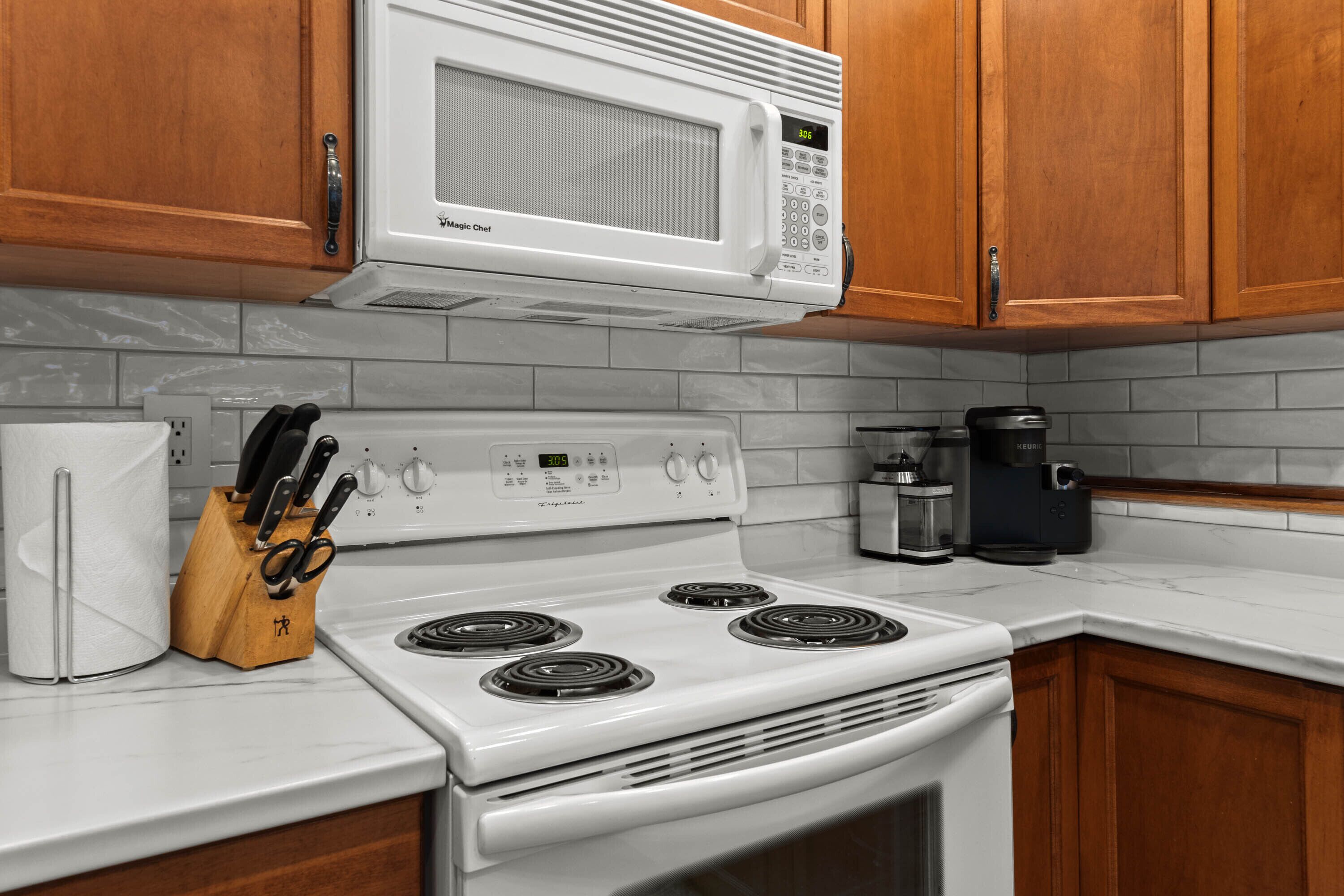 Una cocina con armarios de madera, un microondas blanco, una estufa y una cafetera.