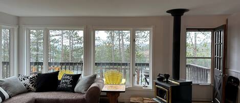 A cozy living room with a sofa, a small table, and a fireplace. Large windows offer a view of the outdoors.