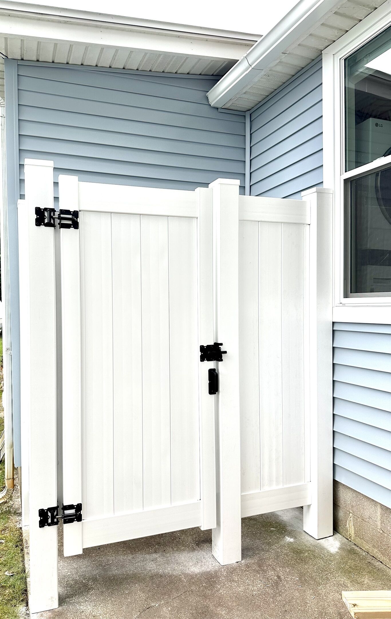 A white gate with black hinges in front of a house with blue siding.