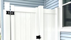 Um portão branco com dobradiças pretas em frente a uma casa com revestimento azul.