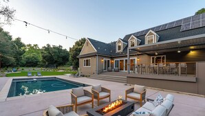 A modern house with a swimming pool, outdoor seating, and solar panels. - Luxe Westside 5BR/3.5BA w/Pool, Hot Tub, FirePit, Movie Room & more. (Templeton)