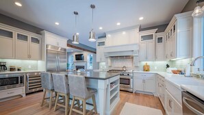 A modern kitchen with white cabinetry, stainless steel appliances, and a central island with bar stools. - Luxe Westside 5BR/3.5BA w/Pool, Hot Tub, FirePit, Movie Room & more. (Templeton)