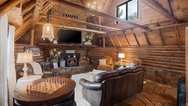 A cozy log cabin interior with a fireplace, leather sofa, and a chess table. - Rustic Cabin with Modern Comfort – The Cuddly Cow in Rudy, AR (Rudy)