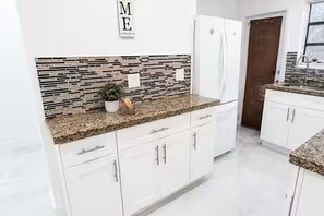 A kitchen with white cabinets, a granite countertop, and a backsplash with a mosaic tile pattern.