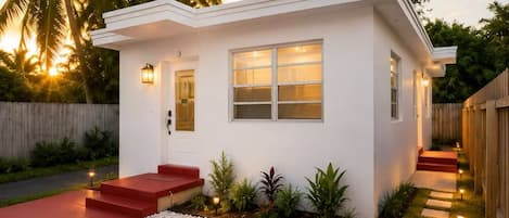Una casa moderna de un piso con un porche delantero rojo, fachada blanca y un pequeño jardín con losetas que conducen a la entrada.