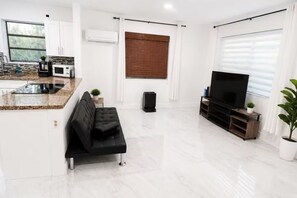 A modern living space with a kitchen, a black sofa, a TV, and a large window.