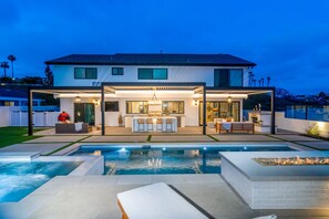 Una casa moderna de dos pisos con una amplia piscina exterior, un patio cubierto y una cocina bien iluminada.