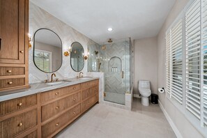 Un baño moderno con tocador de madera, un espejo grande, cabina de ducha de vidrio y un inodoro.