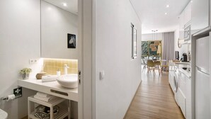 A modern bathroom with a large mirror, white sink, and a small shelf with toiletries.