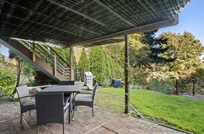 Un patio al aire libre con un área de estar cubierta, una parrilla y una escalera que lleva a un nivel superior.