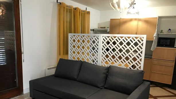 A modern living room with a grey sofa, a wooden cabinet, and a decorative partition. - Beau Appartement Calme et Ensoleillé Parisdisney (Noisy-le-Grand)