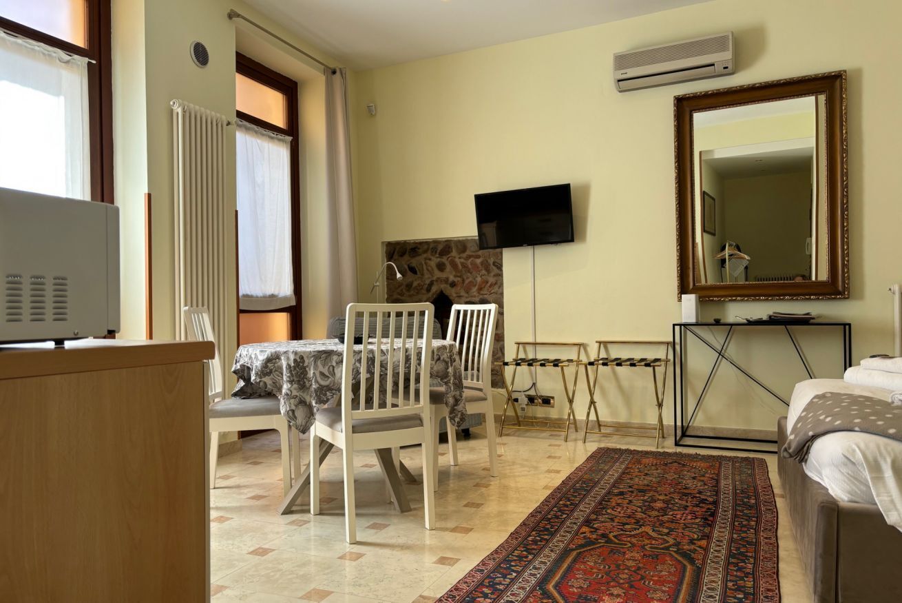 A room with a dining table, chairs, a TV, a bed, a mirror, and a fireplace.