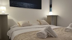 Een net opgemaakt bed met witte lakens en twee kussens, een opgerolde handdoek op het bed, en een afbeelding van een nachthemel op de muur.