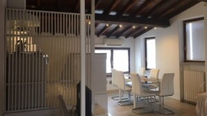 Un comedor moderno con una mesa de vidrio y sillas blancas, techo de madera y un separador blanco.