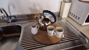 Un lavamanos con grifo de acero inoxidable, una tetera y dos tazas de café sobre un tapete tejido.