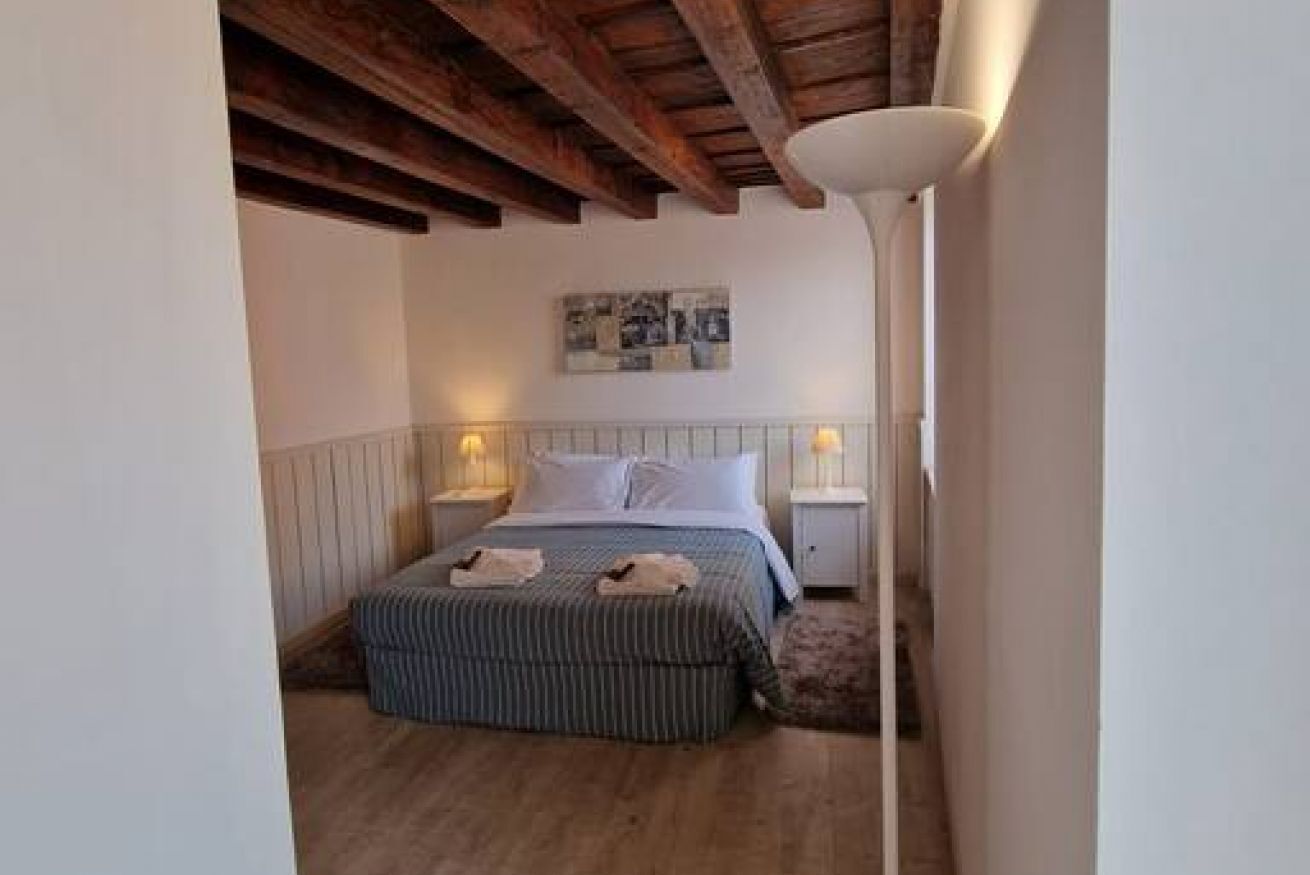 Ein Schlafzimmer mit Holzboden, einem Bett mit gestreifter Bettdecke, zwei Nachttischlampen und einem an der Wand hängenden Kunstwerk.