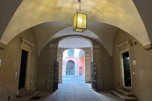 An arched hallway with a hanging light fixture, leading to a courtyard with a gate and a building in the background. - Residenza Montalti - Verona Journeys (VERONA)