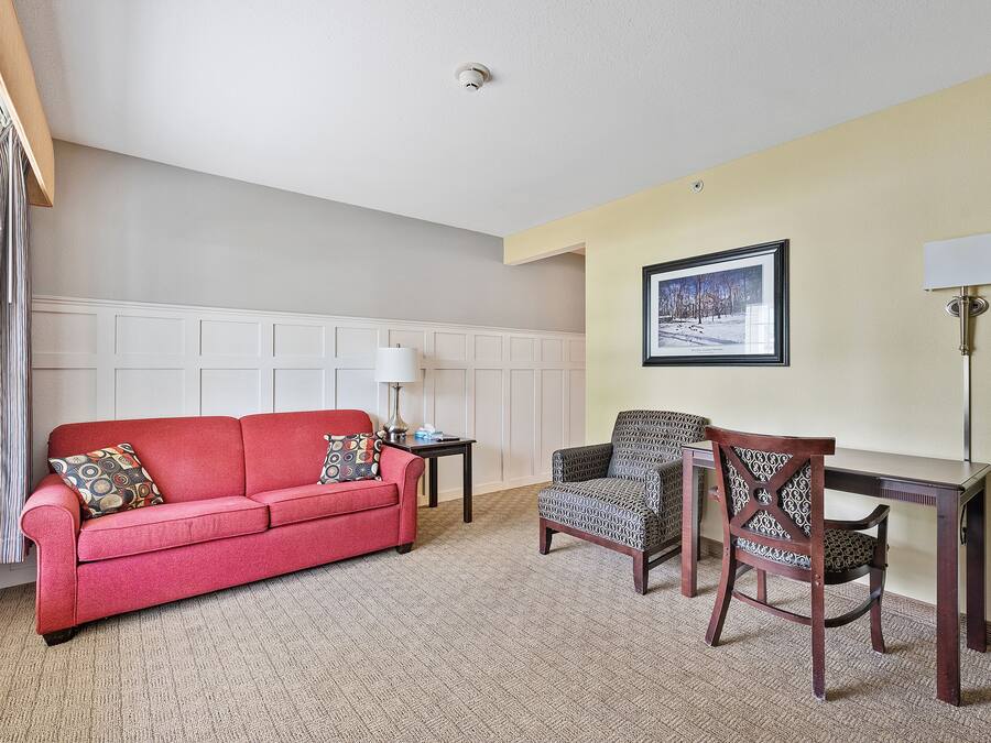 Un salon avec un canapé rouge, un fauteuil à motifs et une petite table sur laquelle se trouve une lampe.