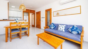 Een woonkamer met een bank, houten stoelen, een salontafel, een eettafel en een plafondventilator.