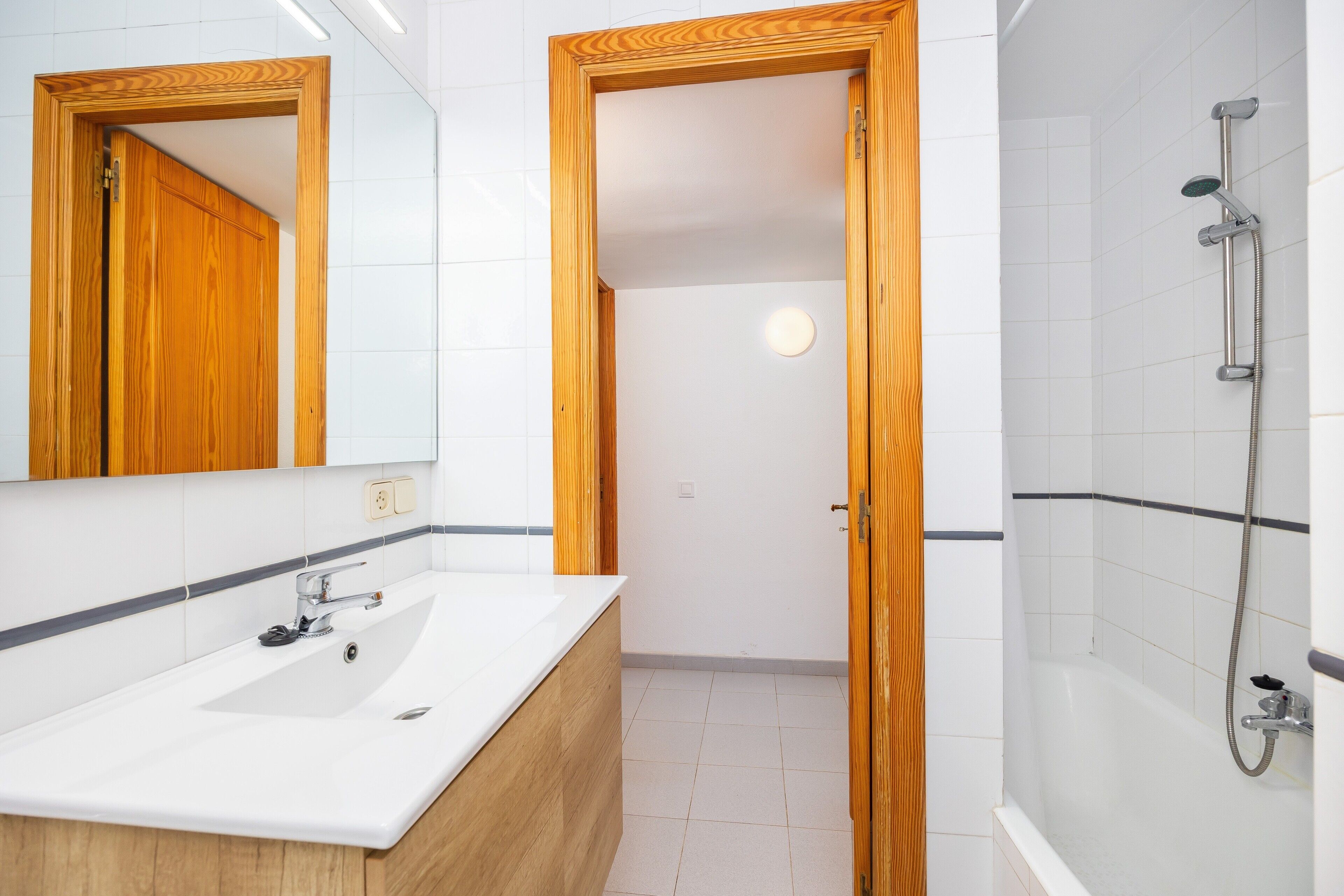 A bathroom with a wooden door, a white sink, and a shower area.