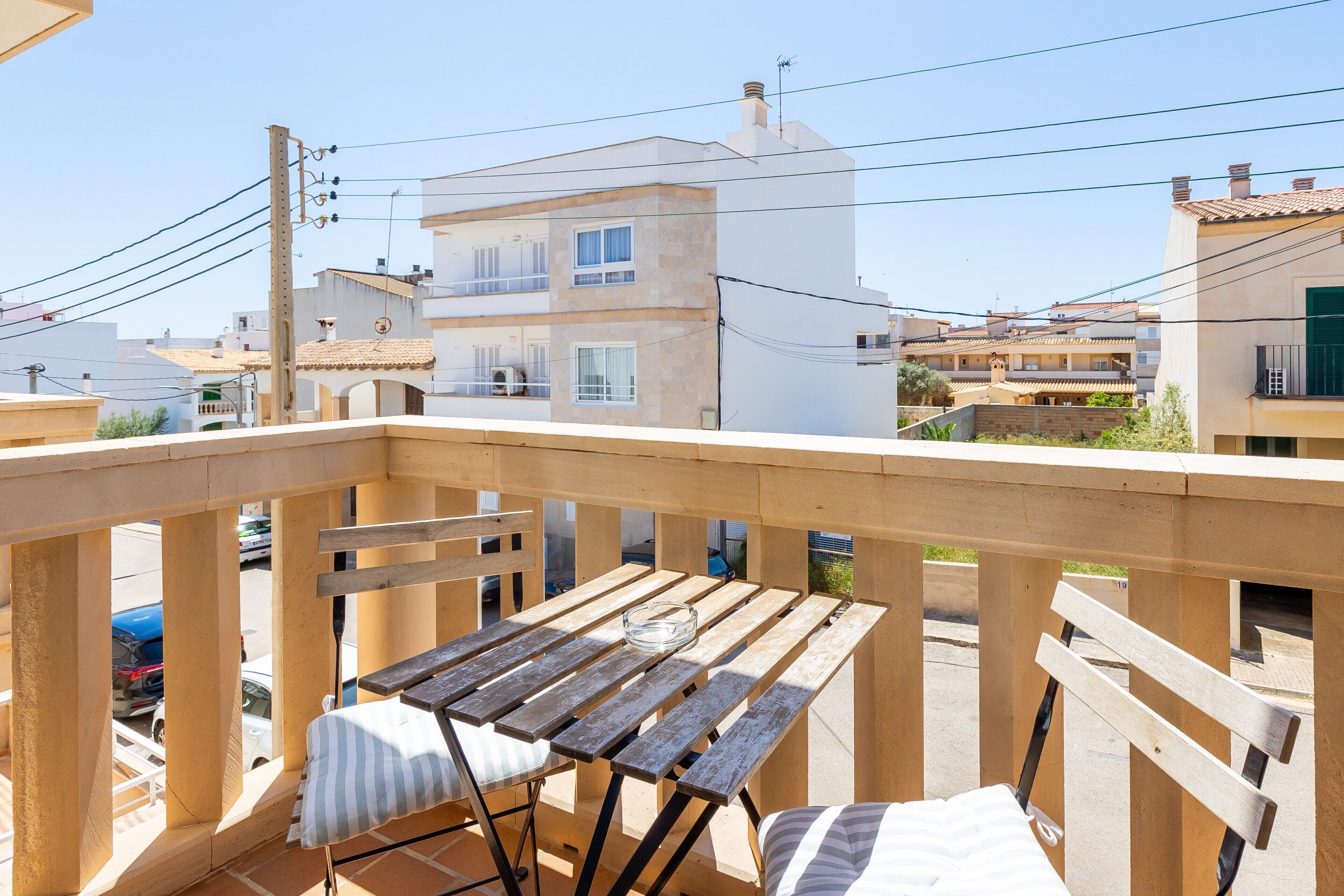 Een balkon met een houten tafel en stoelen, met uitzicht op omliggende gebouwen en een heldere lucht.