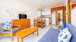 Una sala de estar con un sofá, una mesa de centro de madera, un televisor en un mueble bajo y un comedor con sillas y una mesa.