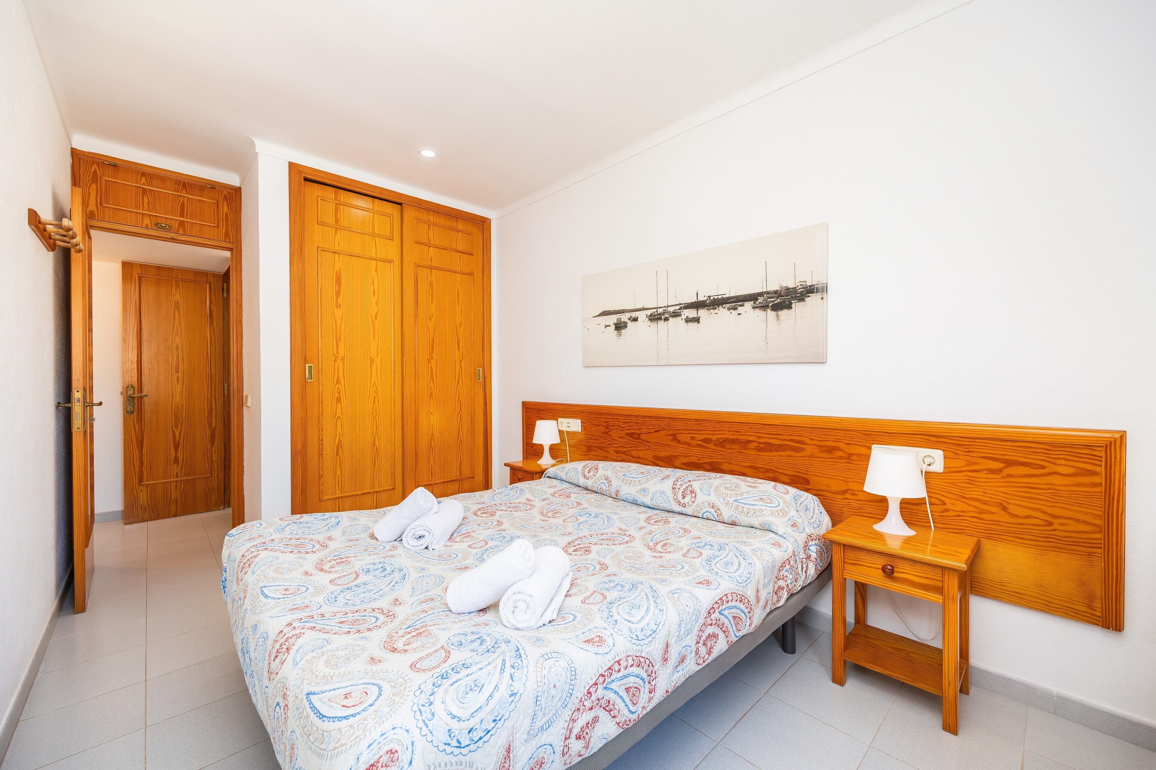 Quarto com cama, guarda-roupa de madeira e mesa de cabeceira com luminária.