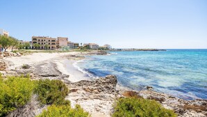 Un hotel frente al mar con playa de arena, mar azul cristalino y un litoral rocoso.