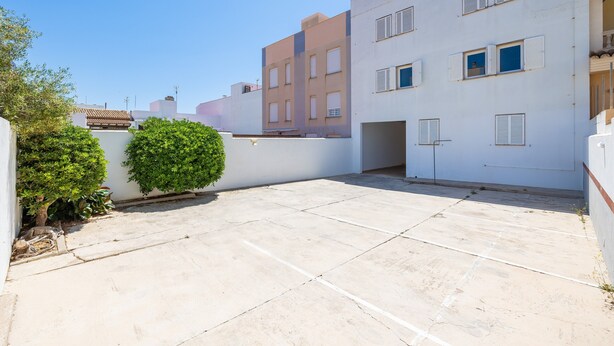 Una terraza en la azotea con un edificio blanco, un pequeño arbusto verde y un cielo azul despejado.