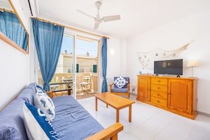 Sala de estar com sofá, mesa de madeira, televisão, poltrona e varanda com cortinas.