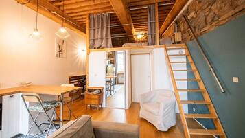 Una habitación estilo loft acogedora, con techo de madera, un comedor con mesa y sillas, una escalera a un nivel superior y un pequeño rincón de descanso con un sillón y un sofá.