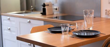 A clean, modern kitchen with a wooden table set for two, featuring black plates, clear glasses, and a water pitcher.