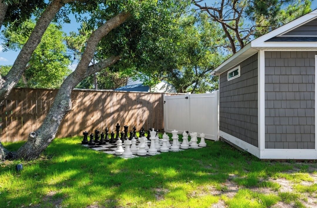 A backyard with a chessboard set up on the grass, a wooden fence, and a shed.