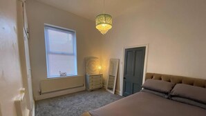 A bedroom with a large bed, a dresser, a mirror, and a chandelier. - Beautiful 3-bed House in Preston (Preston)