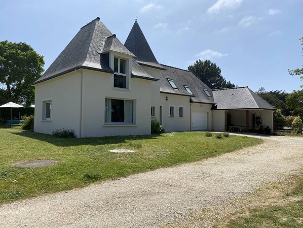 Une maison à deux étages, dotée d’un toit en pente, d’un porche couvert et d’une allée gravillonnée.