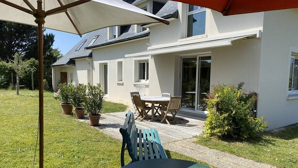 Ein modernes Haus mit Terrasse, einem Tisch mit Stühlen und einem großen Sonnenschirm.