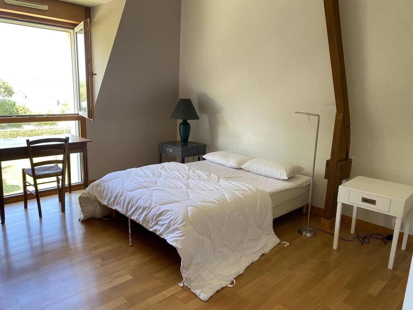 Un dormitorio con una cama, un escritorio, una silla, una lámpara y una mesita de noche.