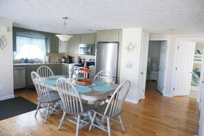 A kitchen with a dining area, wooden flooring, and a window with a checkered curtain.