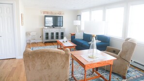 A living room with a television, sofa, and two chairs. There is a window with blinds and a door on the left. - Private access to the beach! Sleeps 9. (Wells)
